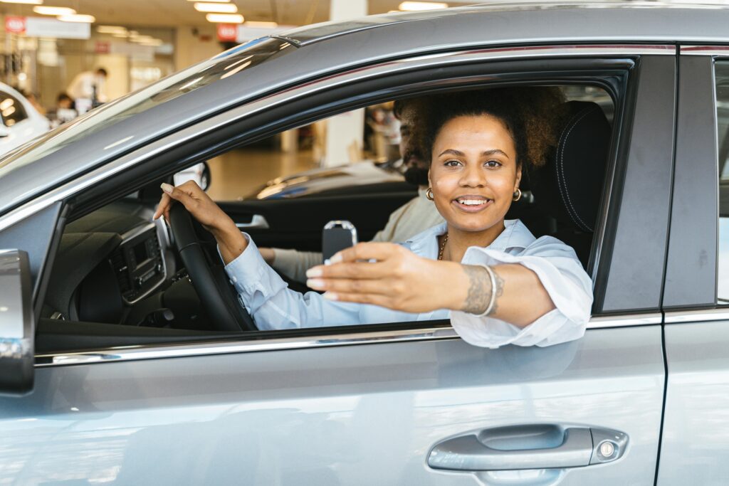 Smiling woman sitting in her new car holding keys, celebrating purchase.